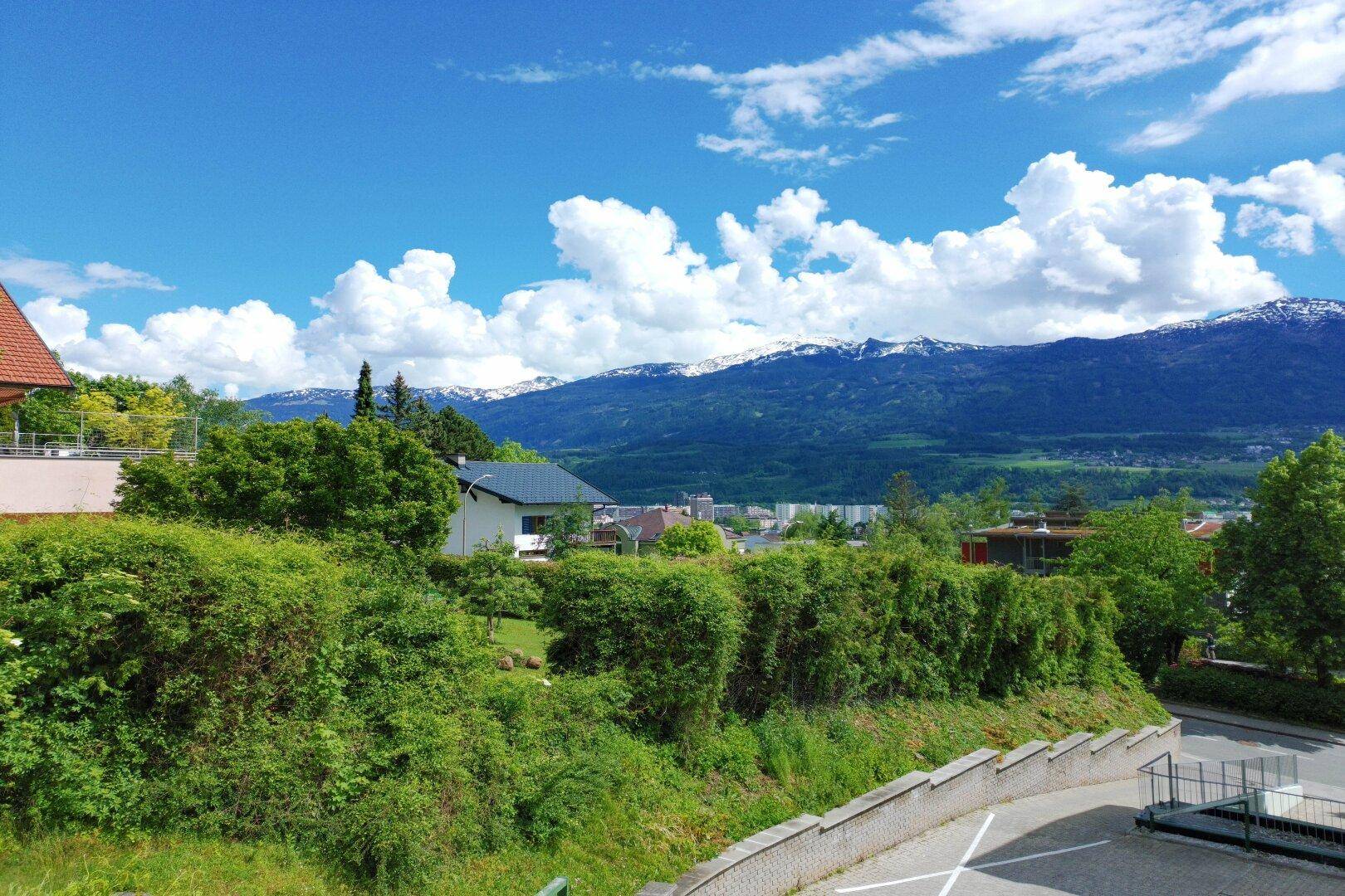 Weitläufiger Panoramablick über eine grüne Landschaft mit schneebedeckten Bergen unter blauem Himmel.