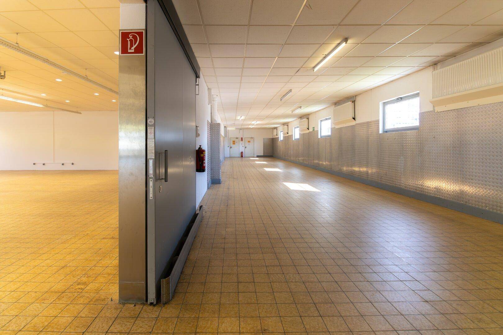 Langer Flur mit Fliesenboden, Metallverkleidung an den Wänden und einer großen Schiebetür.