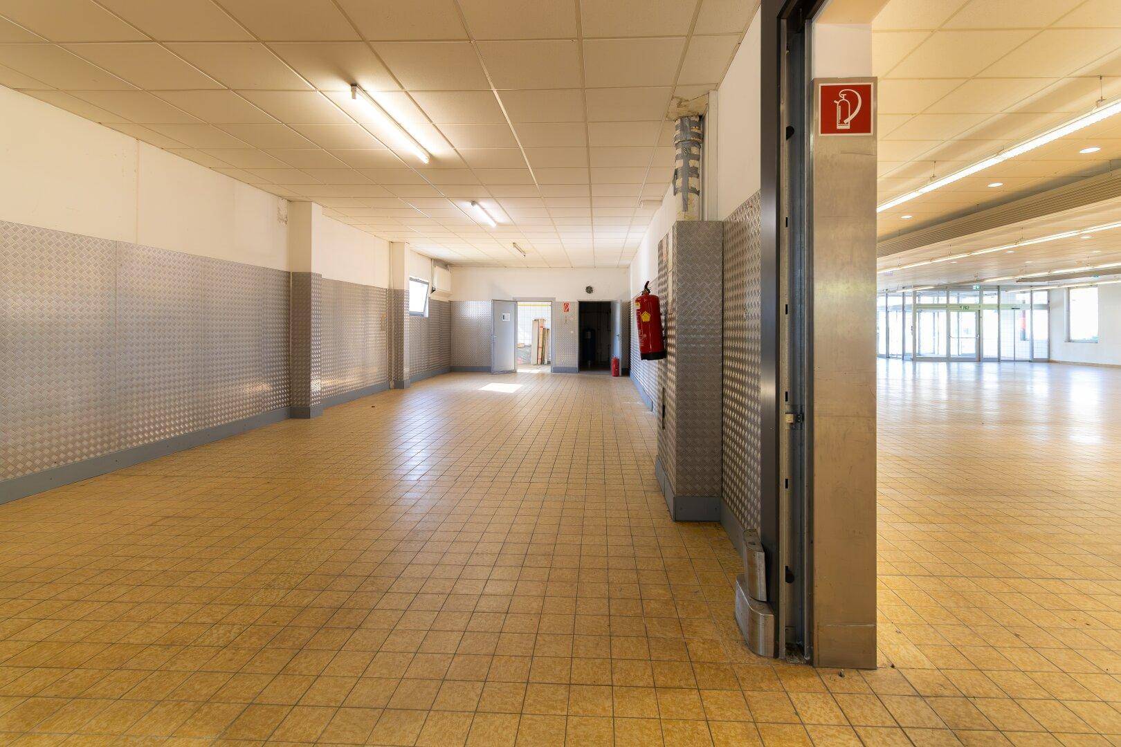 Weiterer Blick in den Flur mit Fliesenboden, Metallwänden und Zugang zu verschiedenen Räumen.