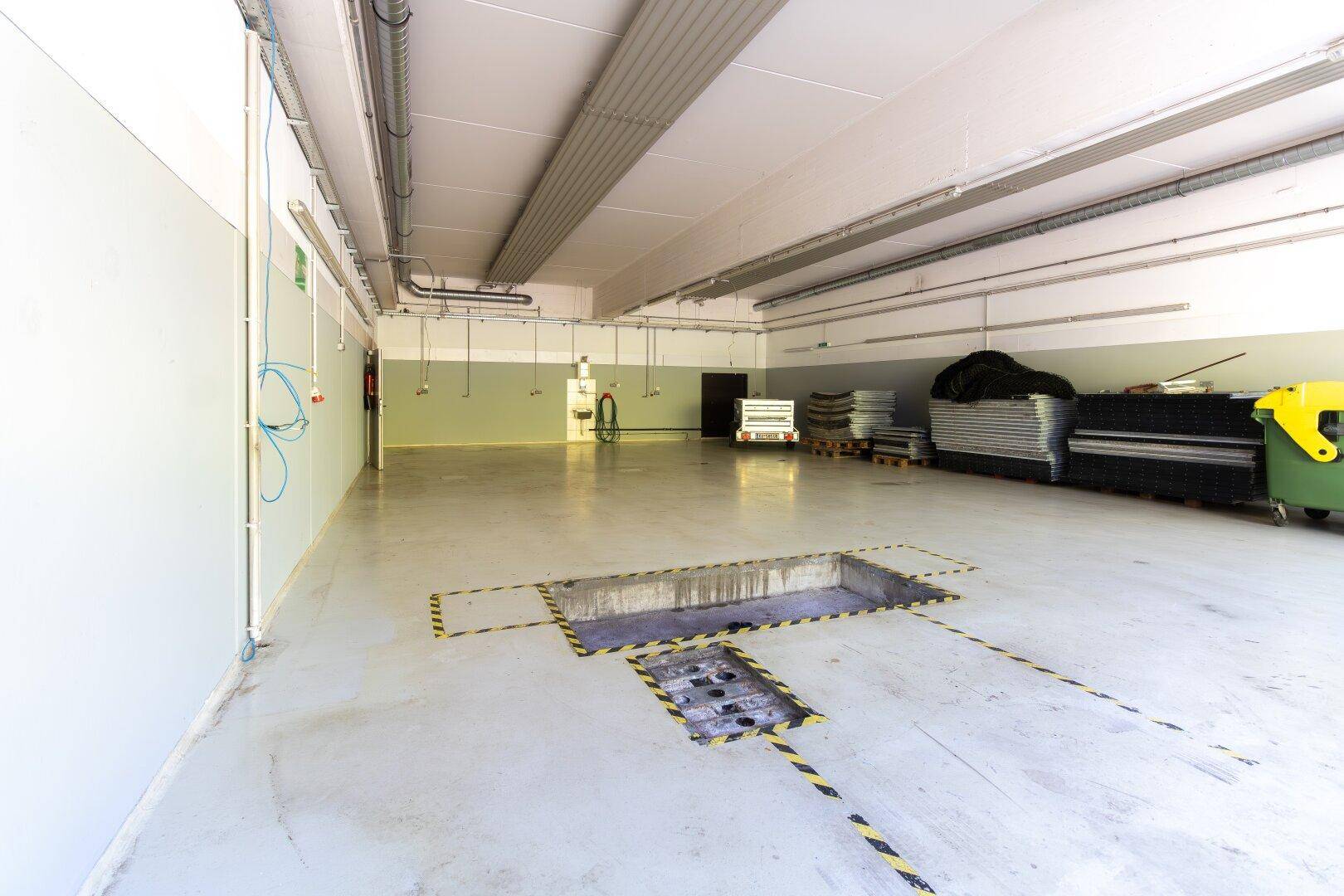 Werkstattbereich mit Betonboden, Wartungsgrube und sichtbaren Installationen an der Decke.