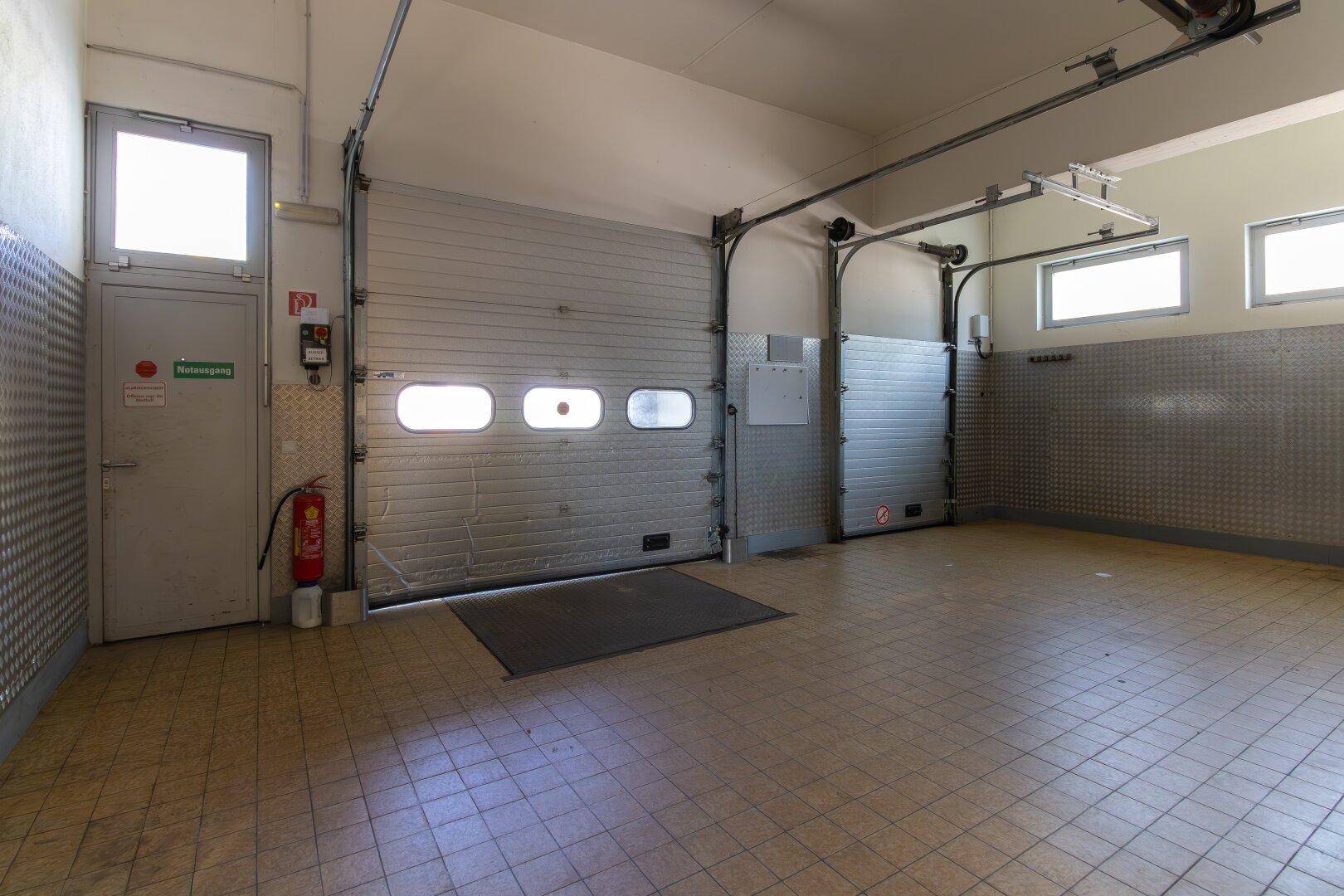 Garagenbereich mit zwei Rolltoren, Fliesenboden und einem Fenster für natürliches Licht.