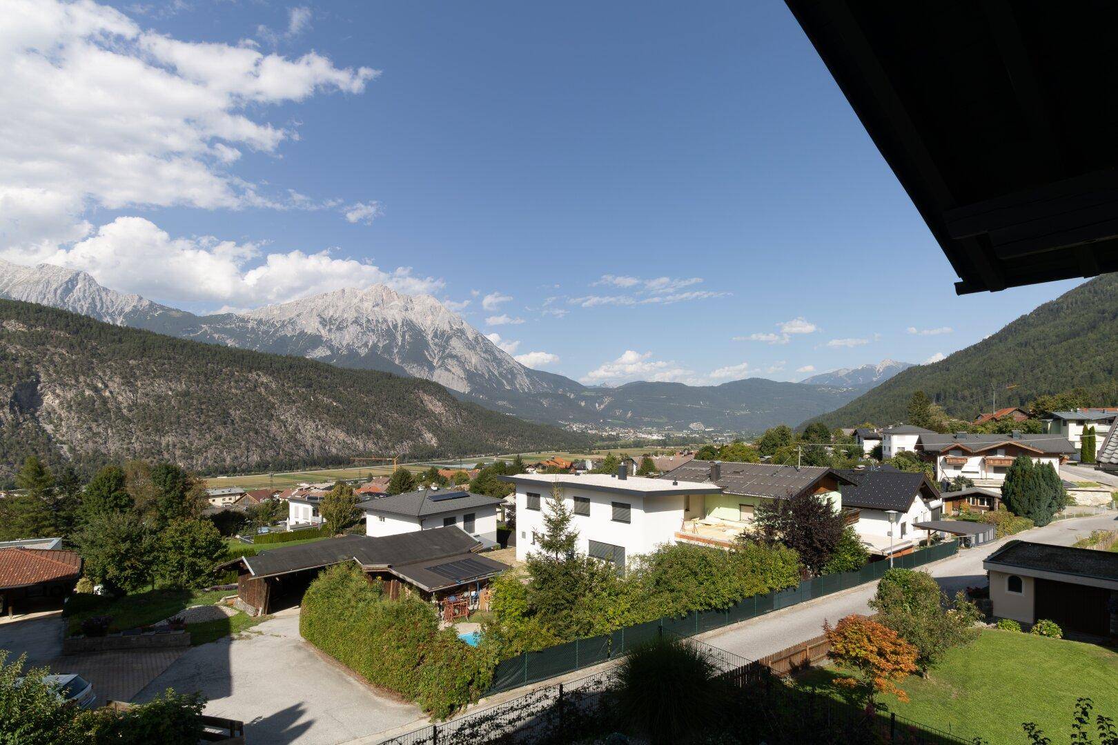 Panoramablick über eine Wohnsiedlung mit grünen Gärten und majestätischen Bergen im Hintergrund.