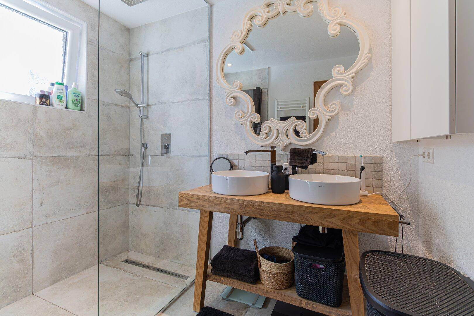 Modernes Badezimmer mit Doppelwaschbecken, großer begehbarer Dusche und einem dekorativen Spiegel.