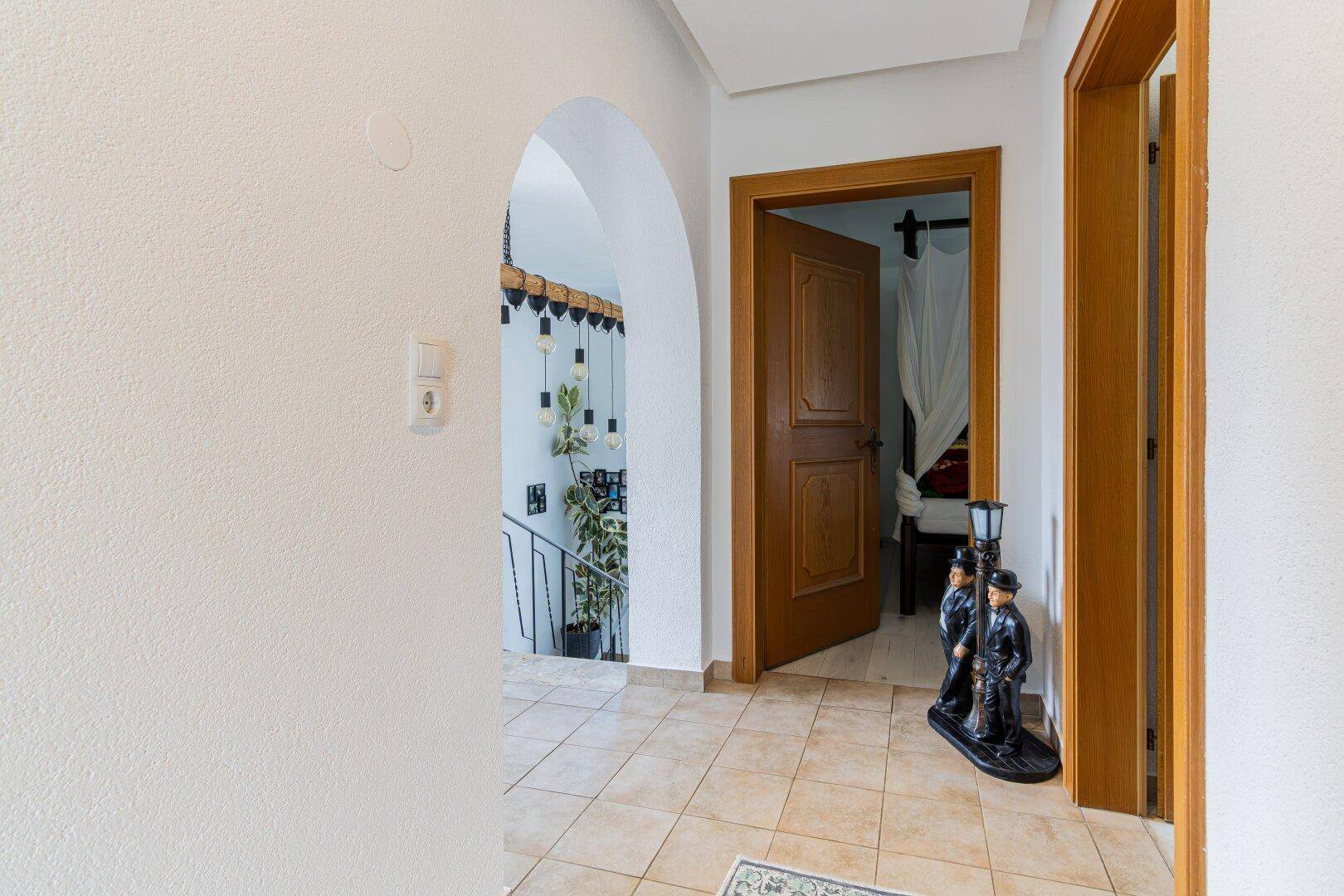 Heller Flur mit Fliesenboden und einem Bogen, der den Blick auf eine Treppe freigibt.