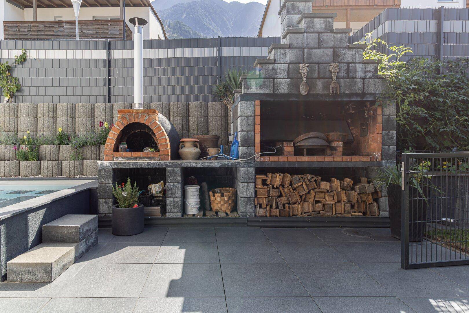 Großer gemauerter Grillbereich mit Pizzaofen und Holzvorrat, ideal für Outdoor-Kochen und Unterhaltung.