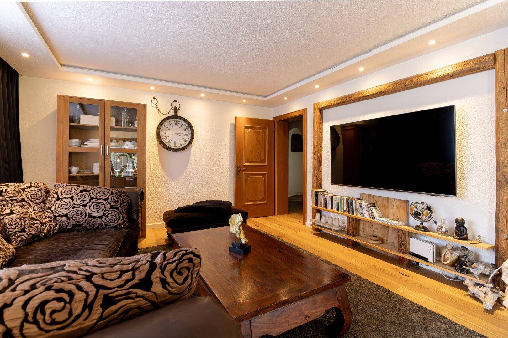 Wohnzimmer mit Holzboden, bequemer Couch und einem großen Fernseher, eingerahmt von Holzbalken.