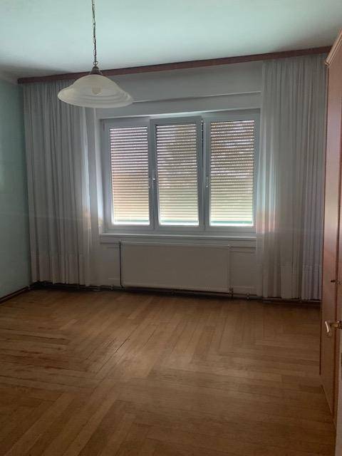 Schlafzimmer mit Fenster, Jalousien und elegantem Holzparkettboden, bietet eine gemütliche Atmosphäre.