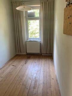 Helles kleines Zimmer mit Fenster, Holzdielenboden und schlichten Wänden, ideal als Schlaf- oder Arbeitszimmer.
