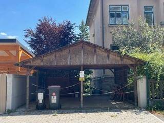 Geräumiger Holzcarport mit zwei Mülltonnen davor, neben dem Hauptgebäude gelegen.