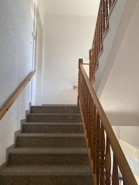 Blick nach oben auf eine Treppe mit Holzgeländer und Granitstufen, die zu den oberen Etagen führt.