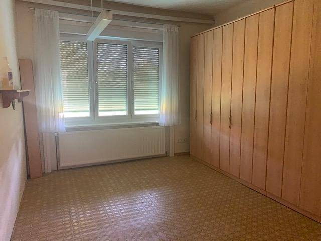 Schlafzimmer mit großem Einbauschrank, Fenster mit Jalousien und gemustertem Bodenbelag.