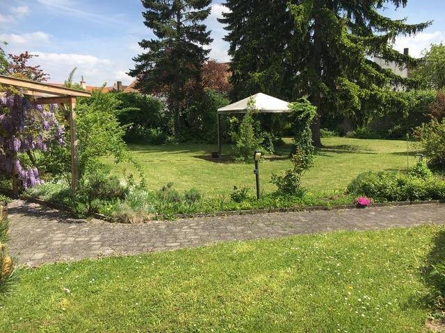 Gepflegter Garten mit gepflastertem Weg, Rasenfläche und einem charmanten Pavillon unter blauem Himmel.