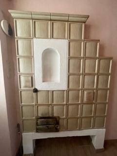 Traditioneller Kachelofen mit beigen Fliesen und weißer Nische, ein zentrales Heizelement.