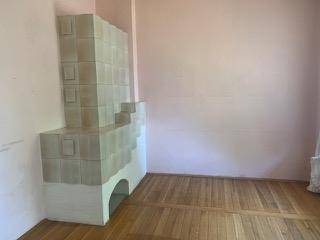 Geräumiges Zimmer mit traditionellem Kachelofen, Holzboden und hellrosa Wänden.