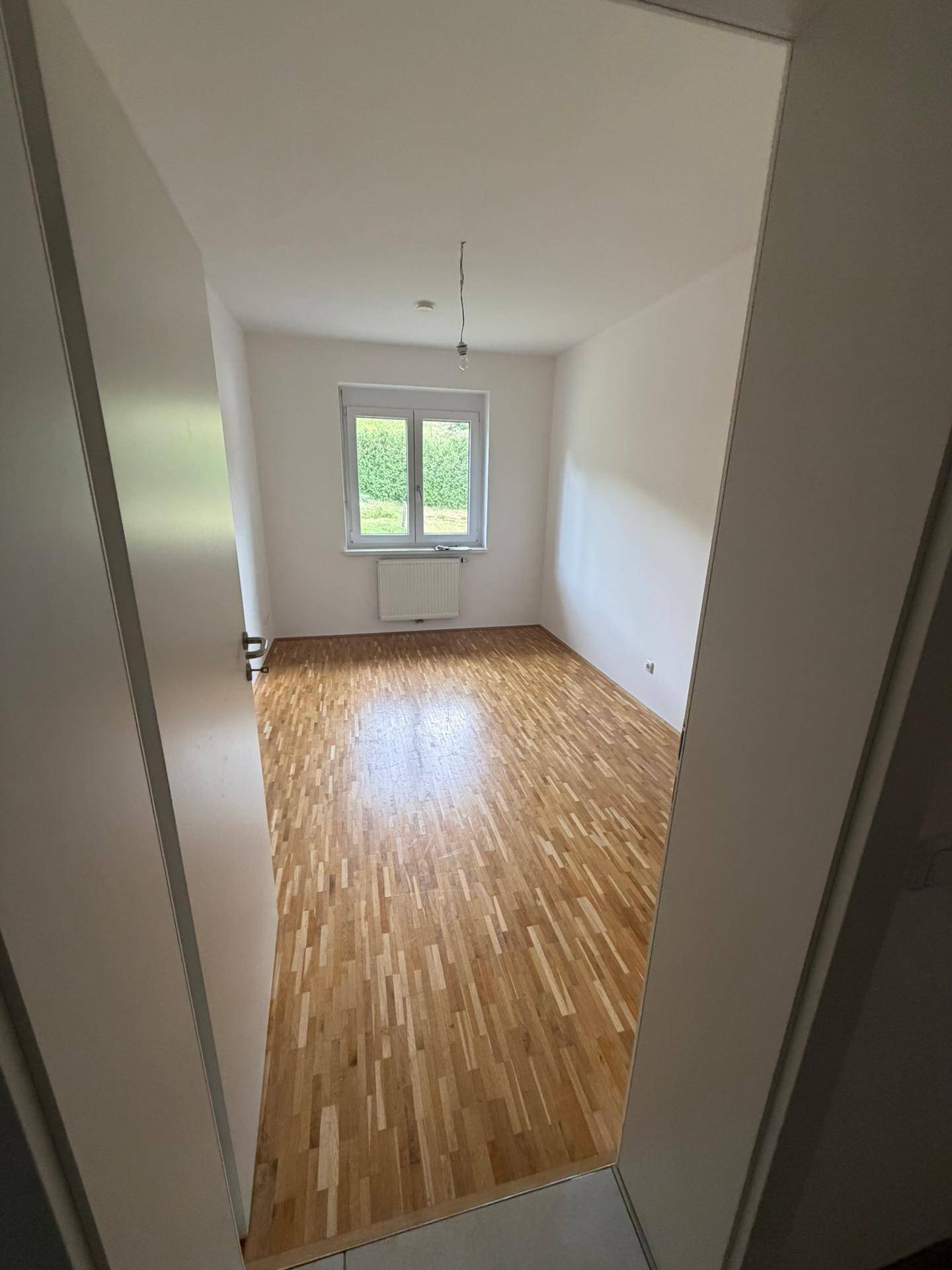 Geräumiges Zimmer mit Parkettboden und Fenster, das eine angenehme Helligkeit schafft.