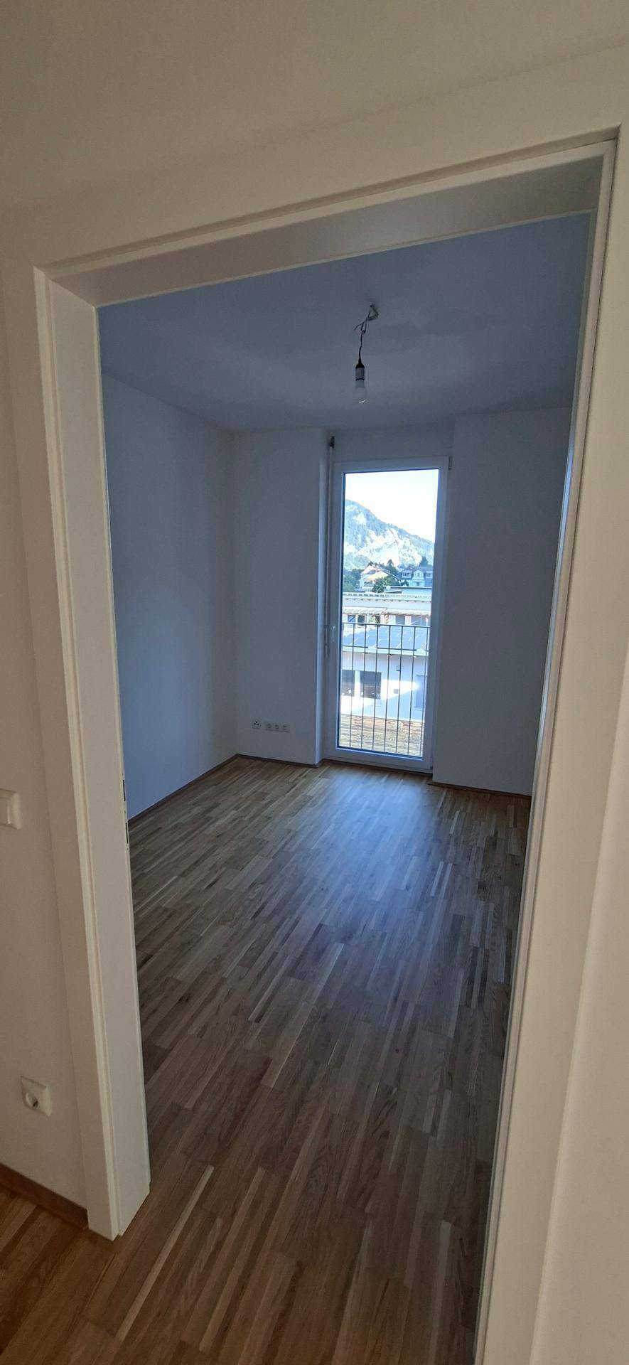Helles Schlafzimmer mit Holzparkettboden, großem Fenster und schönem Bergblick.