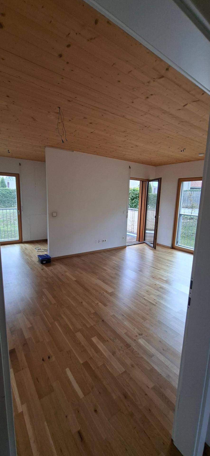 Heller Wohnbereich mit Holzboden und Holzdecke, mit Zugang zu mehreren Balkonen.