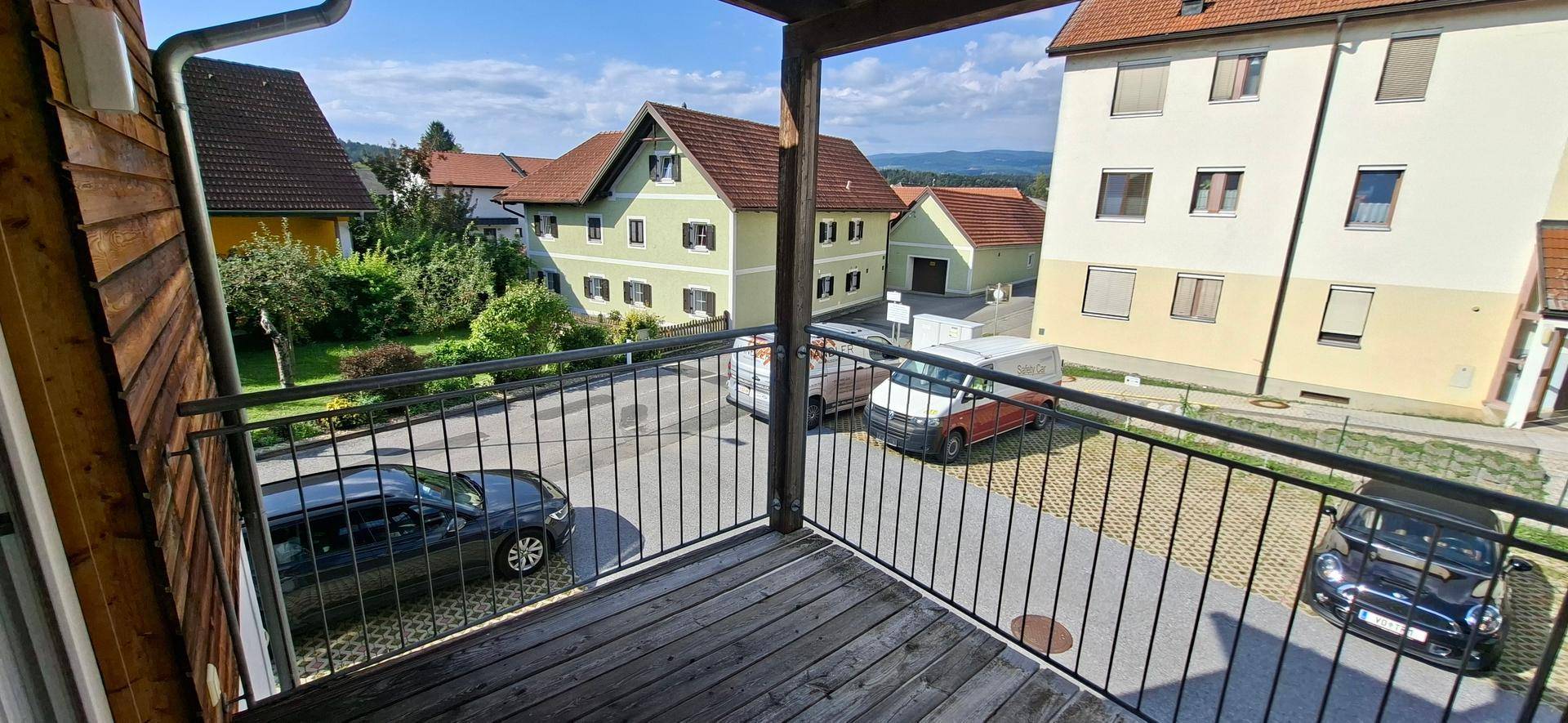 Balkon mit Blick auf die Nachbarschaft, geparkte Autos und eine weite Landschaft im Hintergrund.