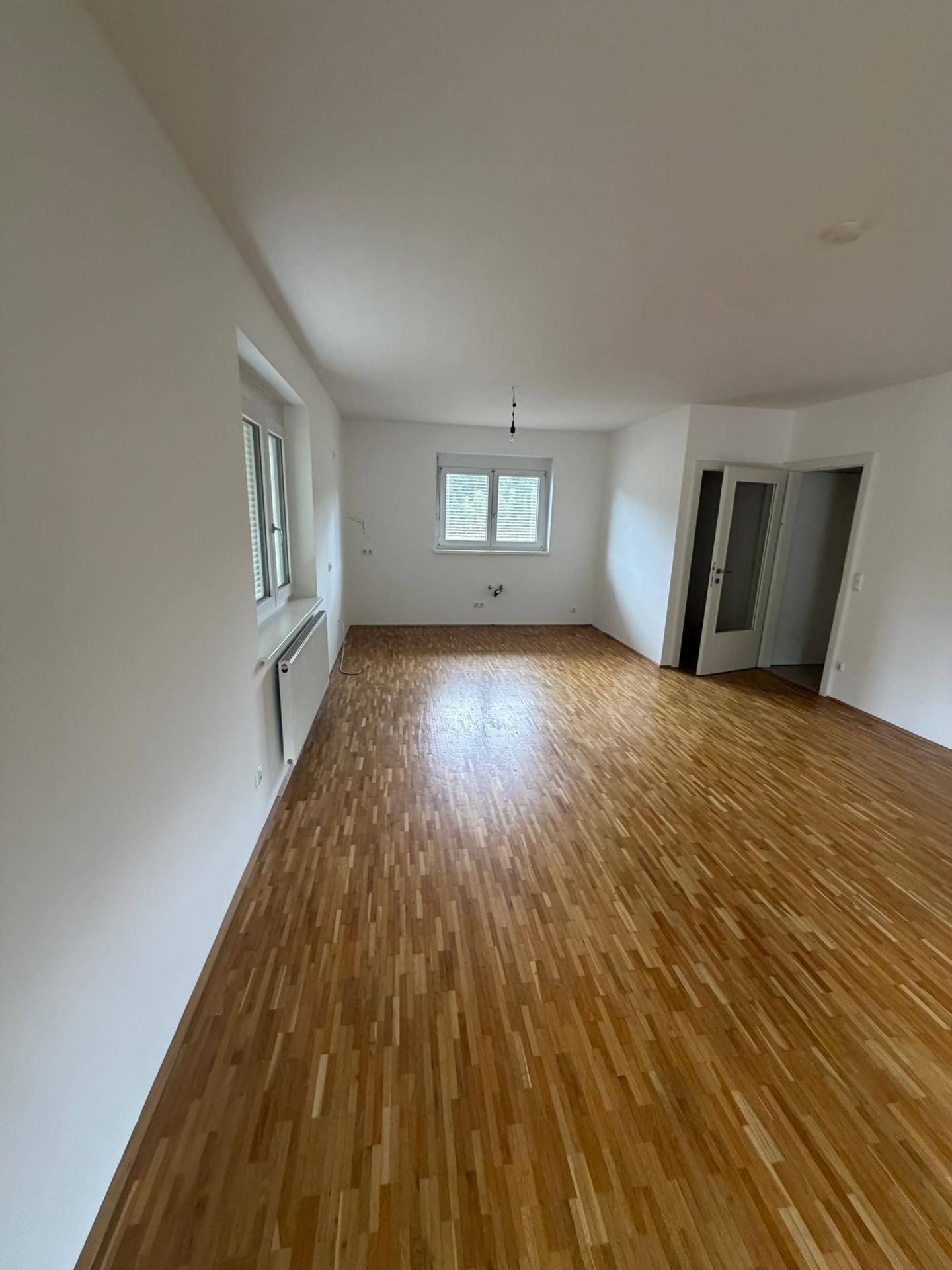 Geräumiges Wohnzimmer mit hellem Parkettboden und weiß gestrichenen Wänden, bereit zur individuellen Gestaltung.