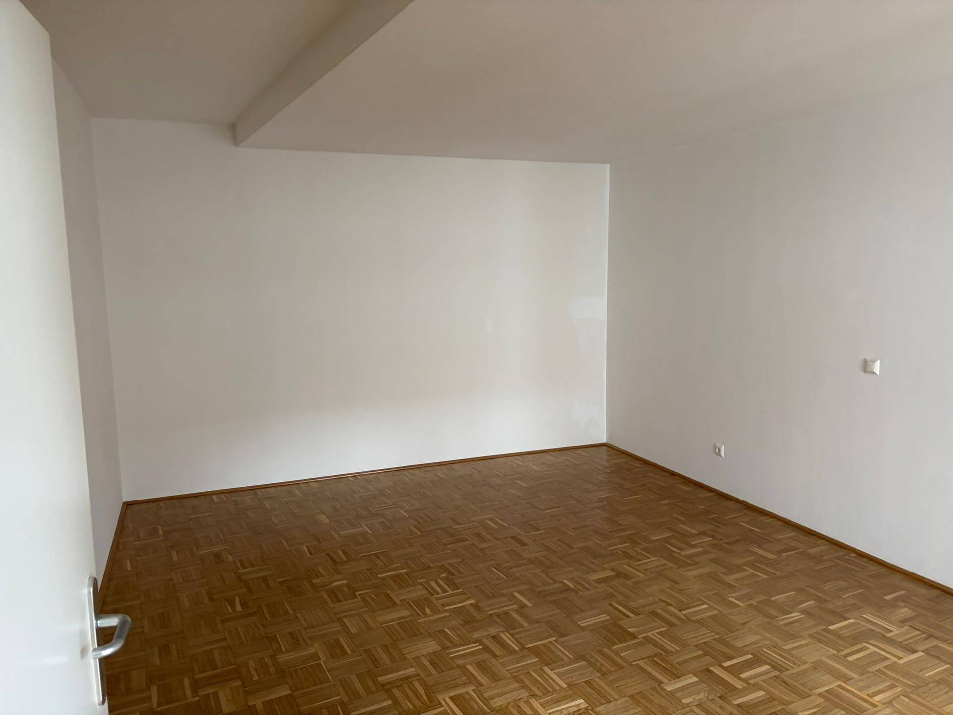 Geräumiges, leeres Zimmer mit hellem Parkettboden und weißen Wänden, bereit zur individuellen Gestaltung.