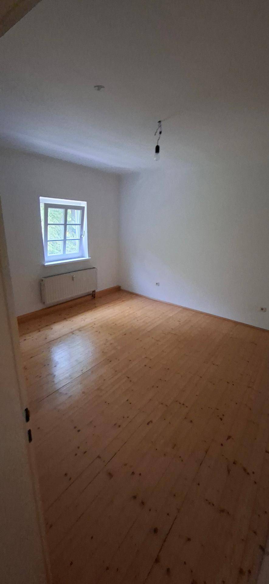 Heller Raum mit Holzplankenboden und einem Fenster, ideal als Schlaf- oder Arbeitszimmer.