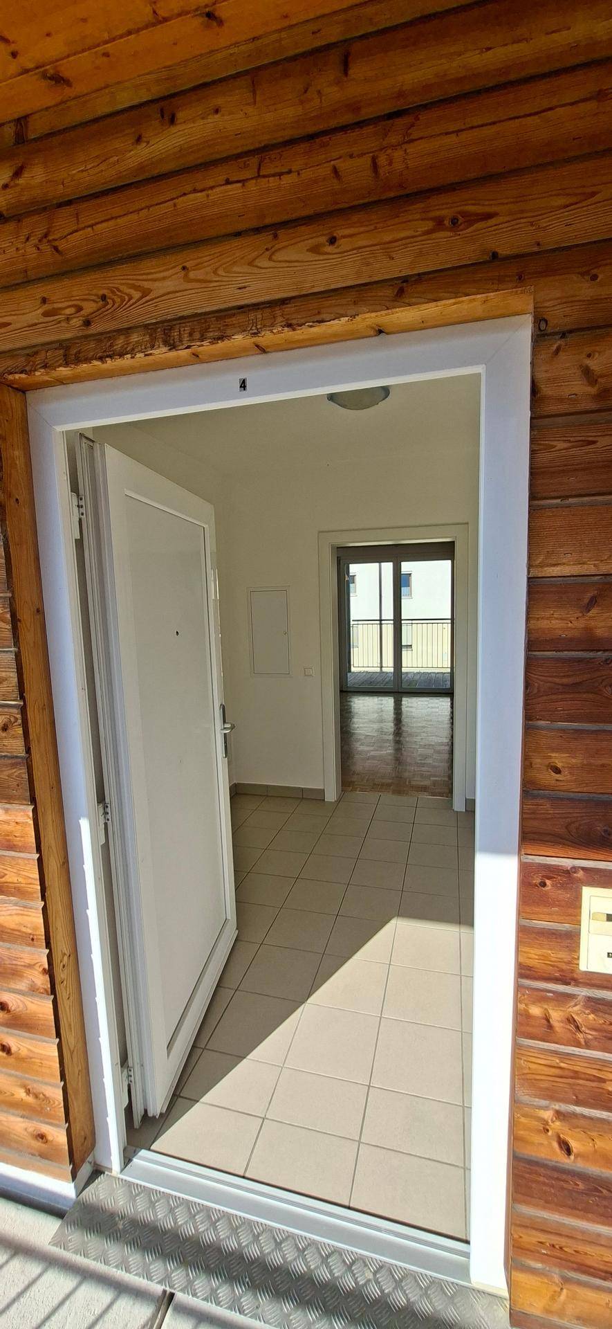 Eingangsbereich mit Fliesenboden, der vom Holzbalkon aus zugänglich ist und in die Wohnung führt.