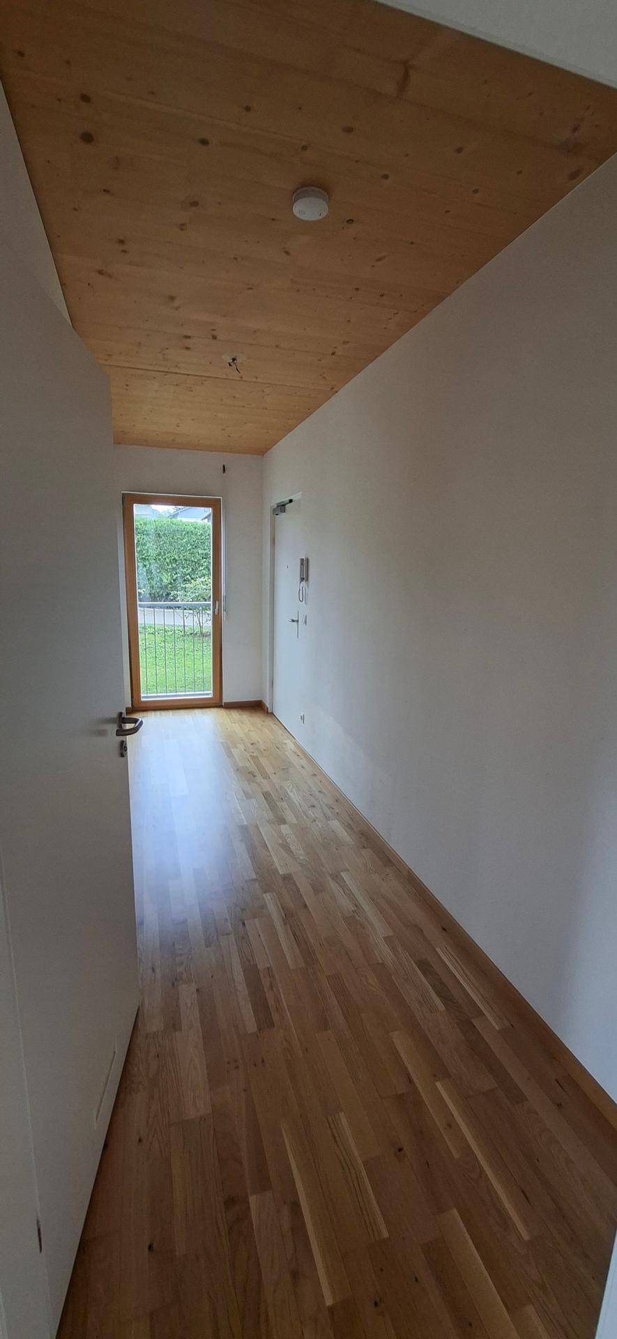 Langer, heller Flur mit Holzboden und Holzdecke, der zum Balkon oder Garten führt.