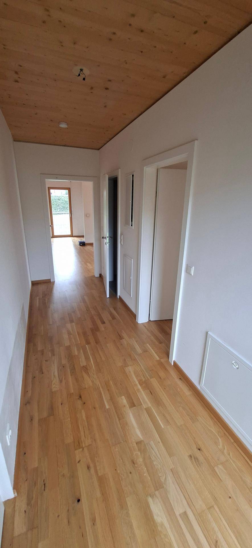 Heller Flur mit Holzparkettboden und Holzdecke, der zu weiteren Räumen führt.