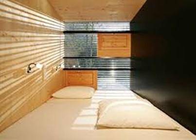 Kleines Schlafzimmer oder Schlafkapsel mit Holzwänden, einem Bett und einem Fenster mit Jalousien.