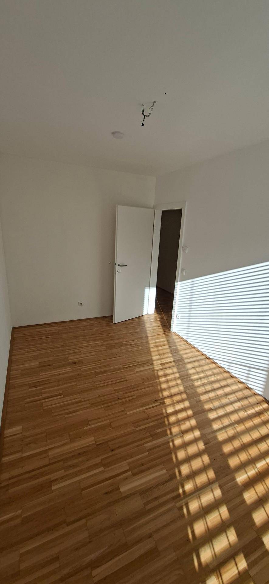 Sonniger Raum mit Holzparkettboden und hellen Wänden, ideal als Schlaf- oder Arbeitszimmer.