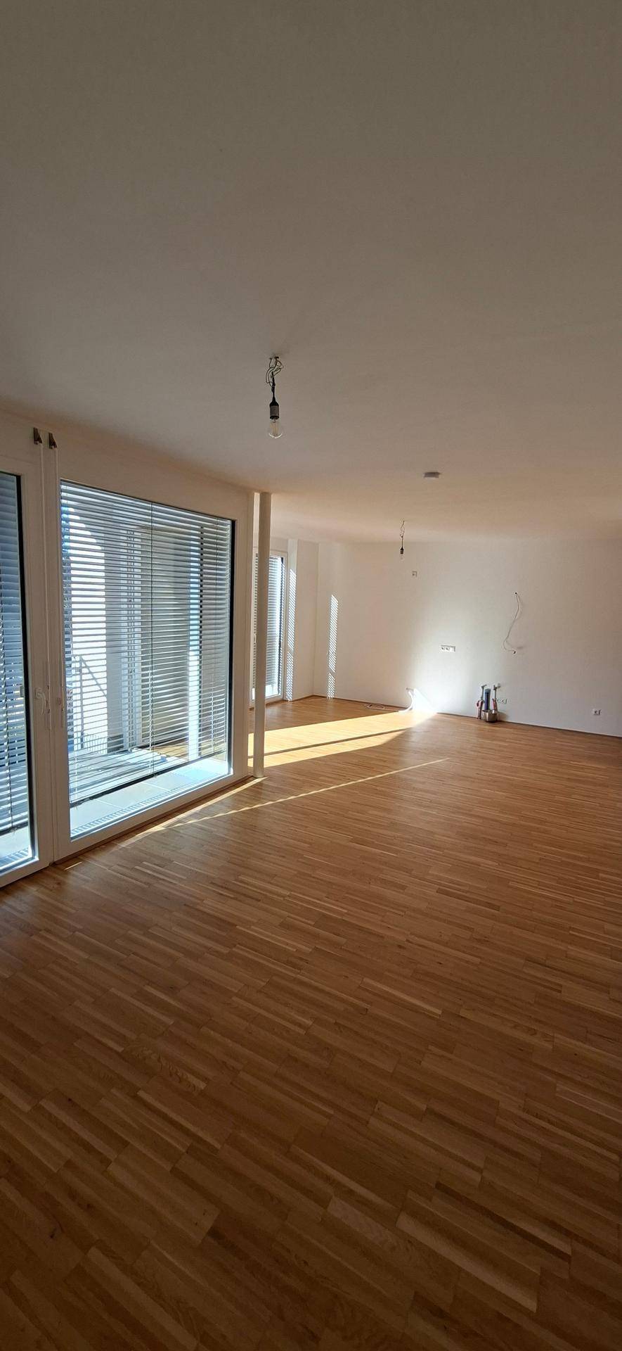 Helles und geräumiges Wohnzimmer mit Holzparkettboden und großen Fenstern für viel Tageslicht.