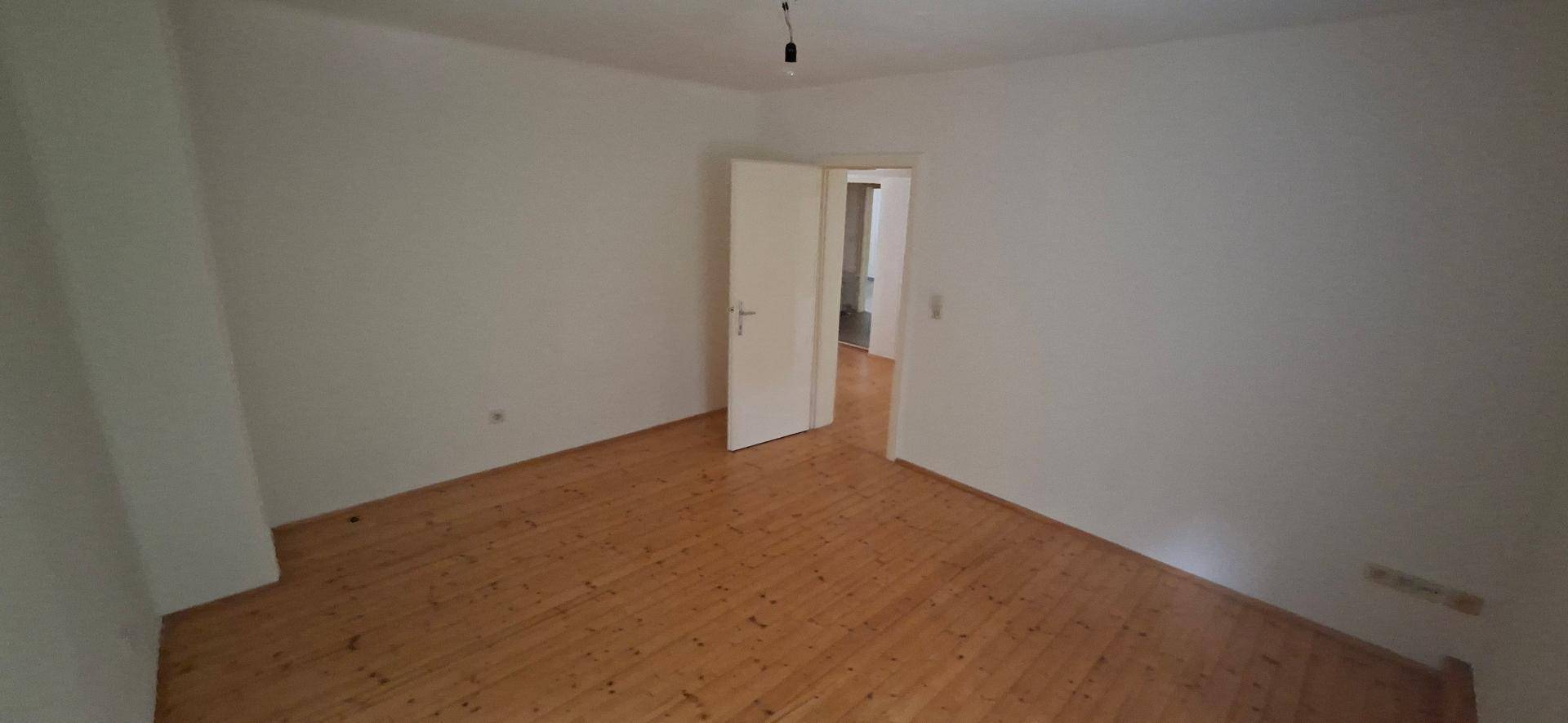 Geräumiger, heller Raum mit Holzplankenboden und einer Tür, bietet vielseitige Nutzungsmöglichkeiten.