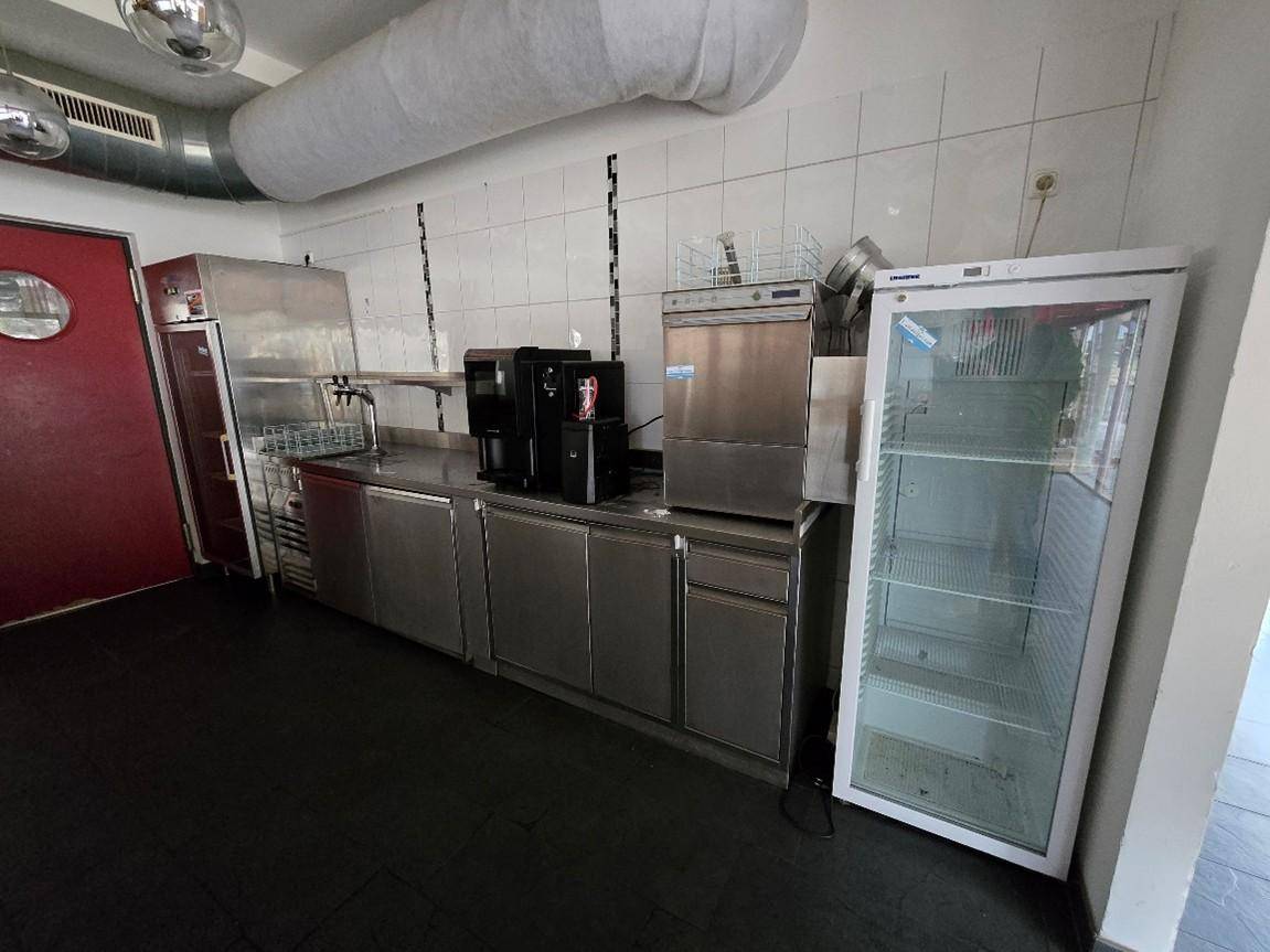 Teil einer professionellen Küche mit Edelstahloberflächen, Kaffeemaschinen, Geschirrspüler und Kühlschrank.