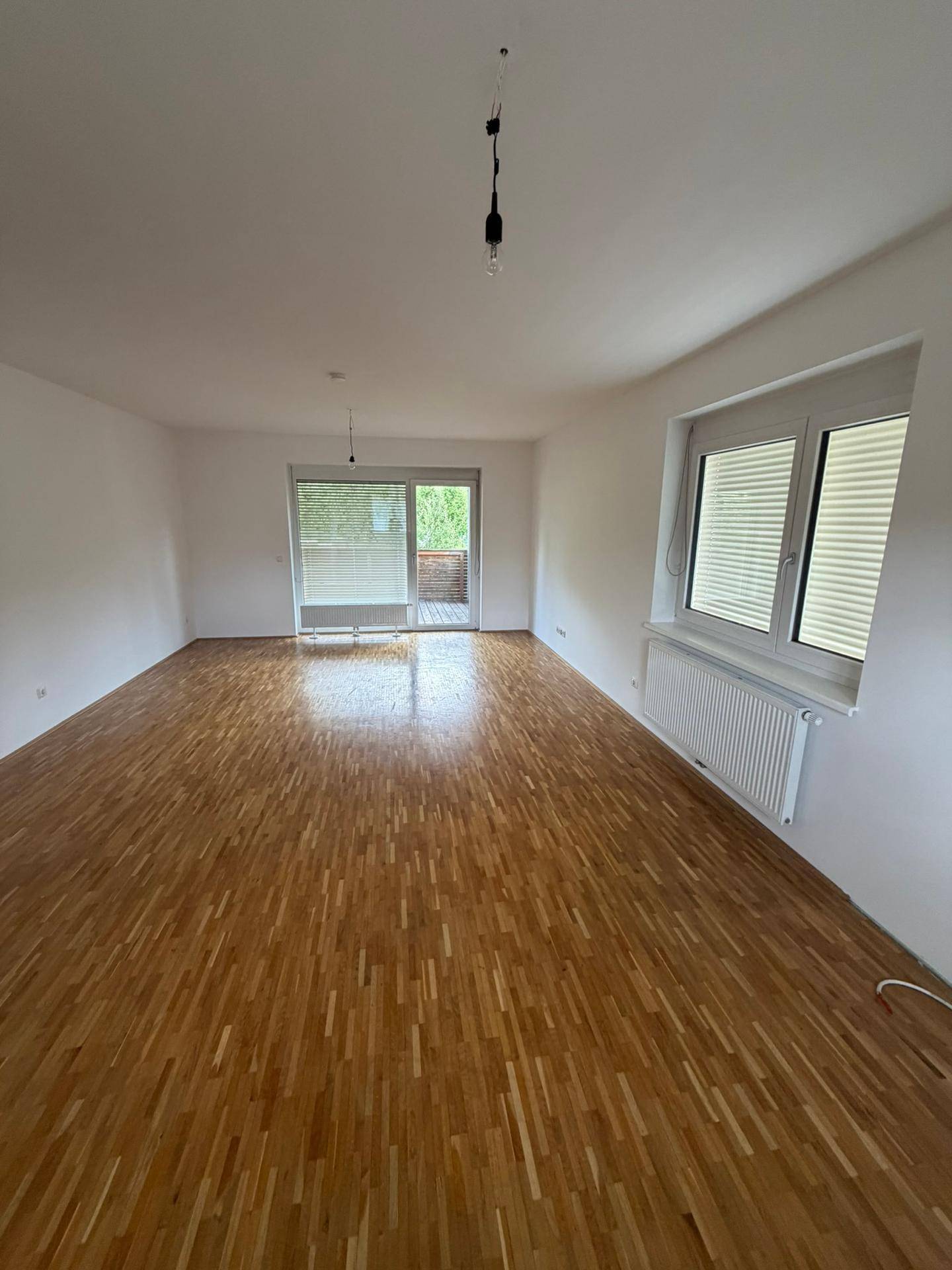 Helles Wohnzimmer mit Parkettboden und Zugang zu einem Balkon, der viel Licht hereinlässt.