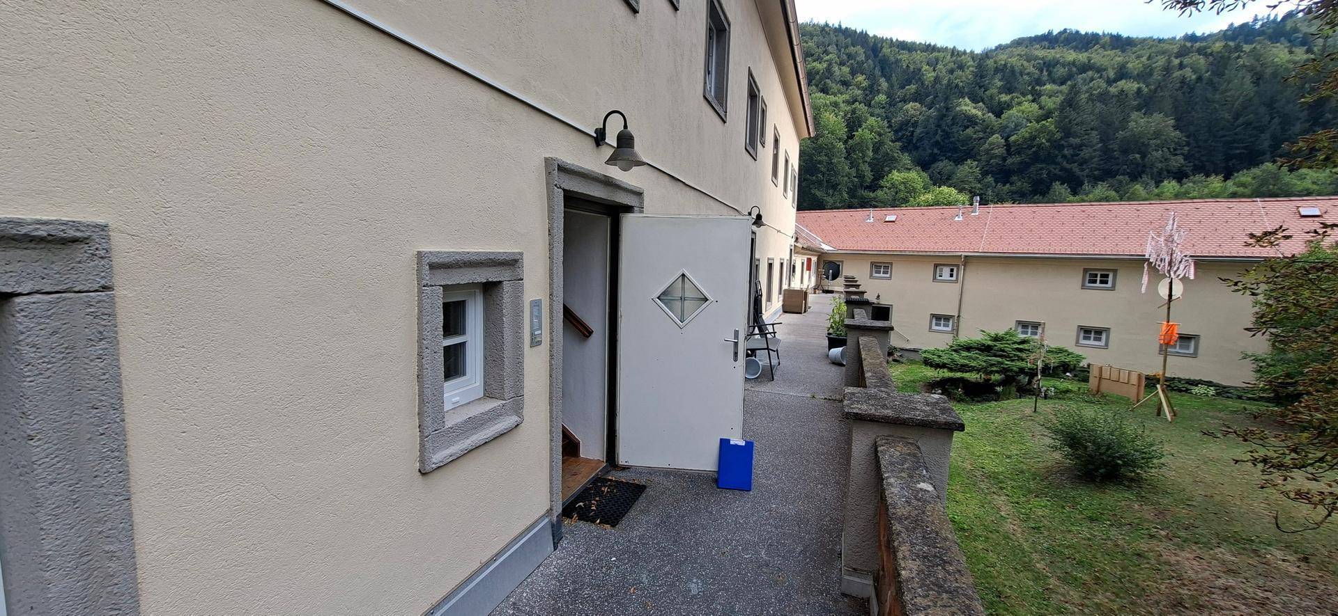 Eingangsbereich eines Gebäudes mit offener Tür und einem Weg entlang der Fassade.