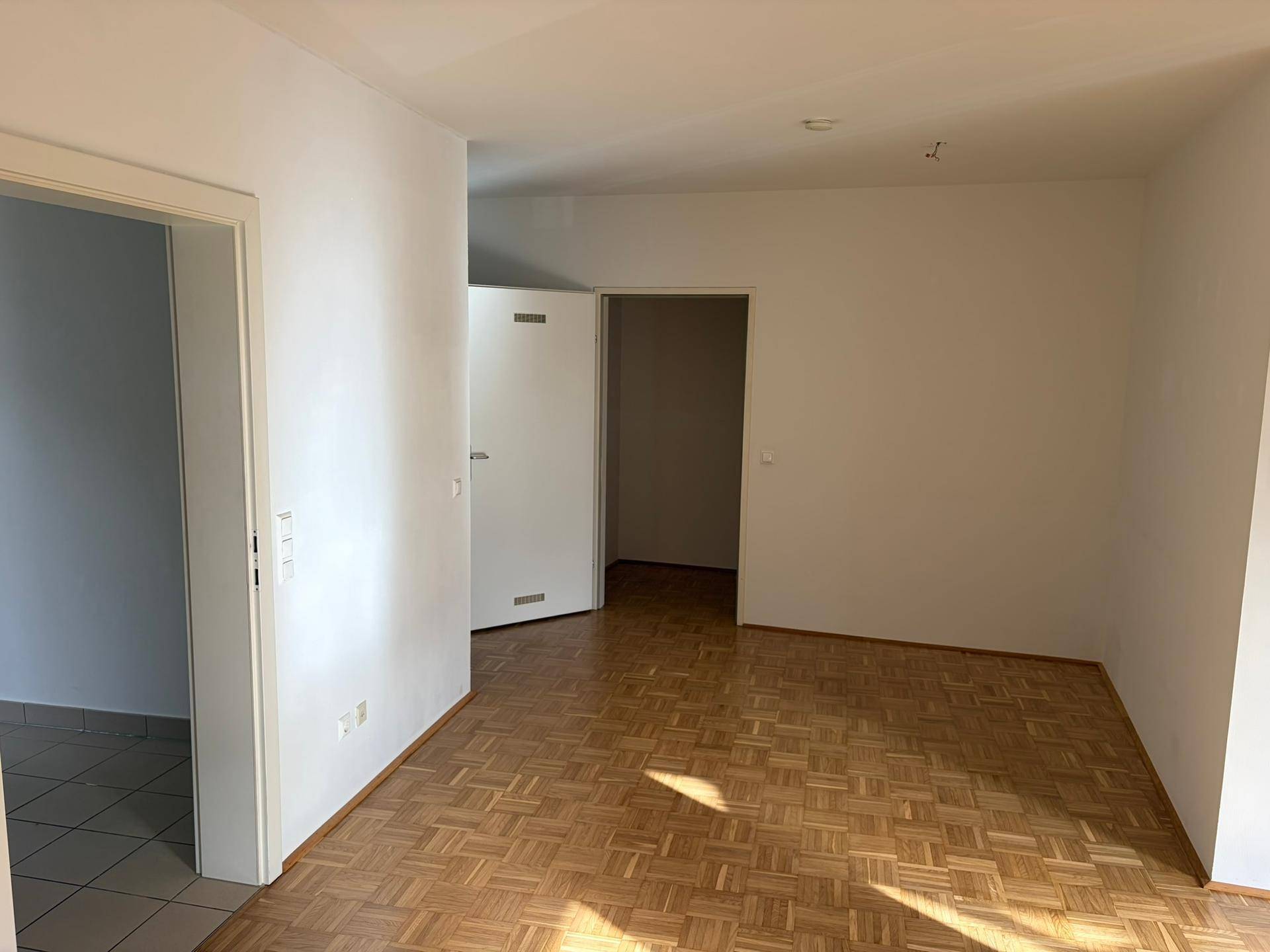 Heller Wohnbereich mit Parkettboden und offenen Durchgängen zu weiteren Zimmern der Wohnung.