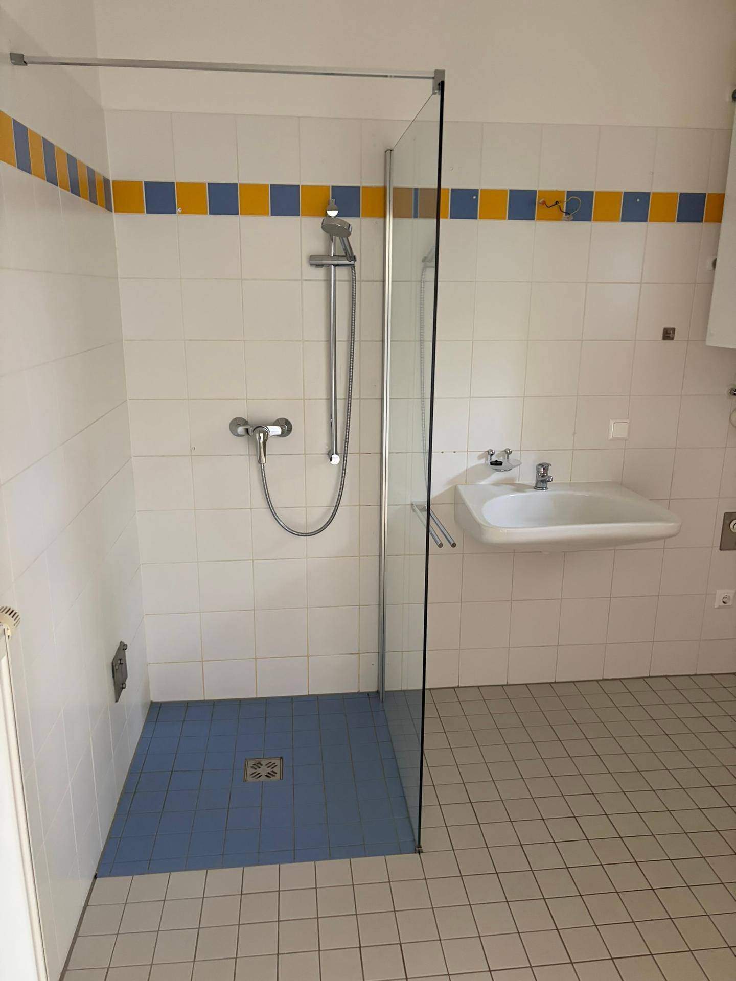 Modernes Badezimmer mit begehbarer Dusche, weißen Fliesen und farbigen Akzenten an der Wand.