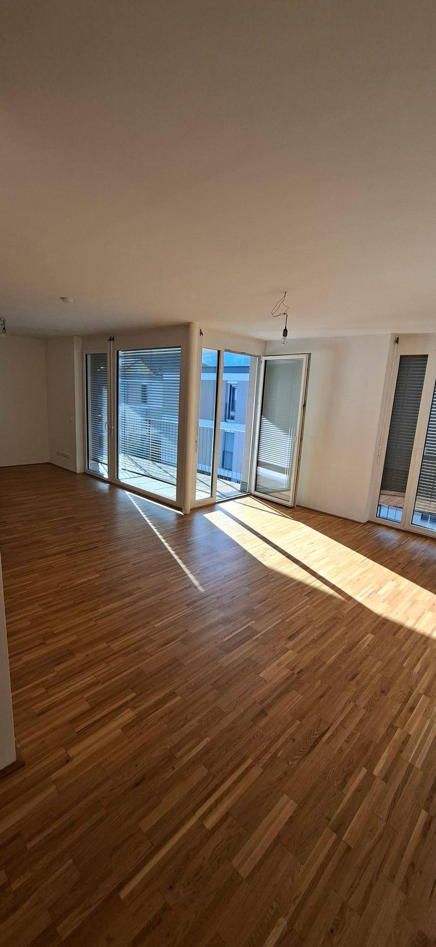 Großes, lichtdurchflutetes Wohnzimmer mit Holzparkettboden und Zugang zum Balkon.