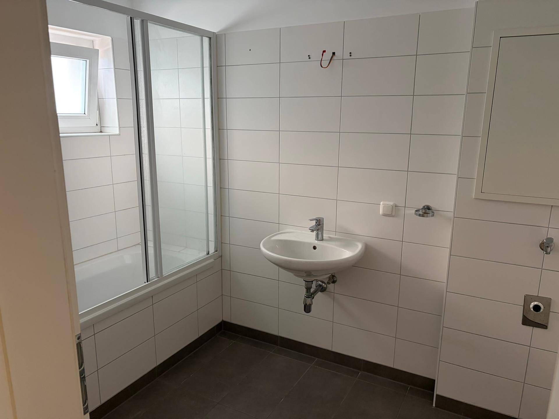 Modernes Badezimmer mit weißen Fliesen, Waschbecken und einer Duschkabine mit Glaswand.
