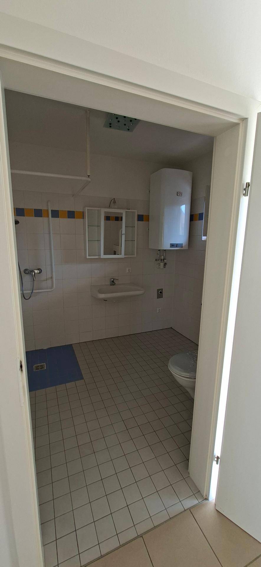 Badezimmer mit Fliesenboden, Dusche, Waschbecken und WC, in einem älteren, funktionalen Zustand.