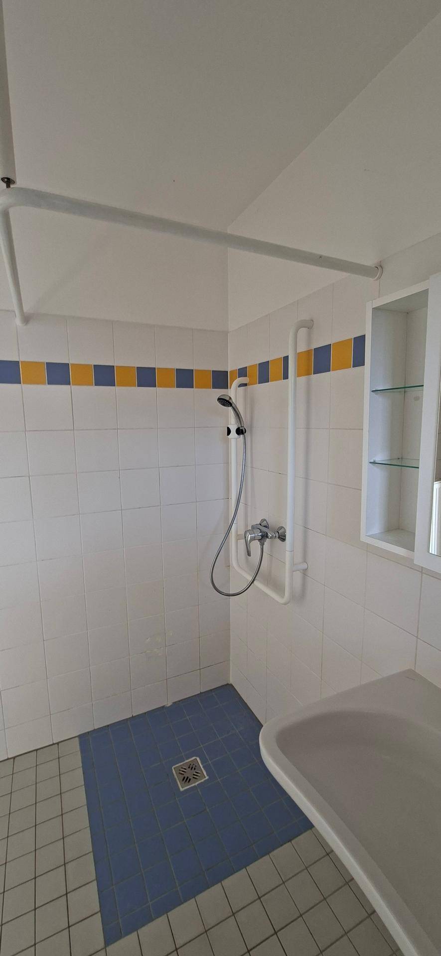 Duschbereich im Badezimmer mit blauen Bodenfliesen und weißen Wandfliesen, ausgestattet mit Duschstange.
