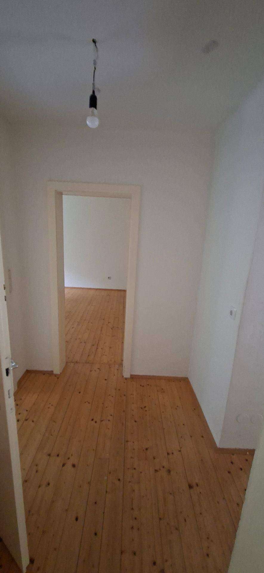 Heller Flur mit Holzplankenboden und Blick in einen angrenzenden Raum, der viel Licht erhält.
