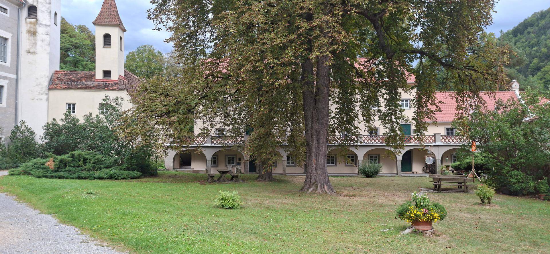 Weitläufiger Innenhof mit altem Baumbestand, historischen Gebäuden und Sitzgelegenheiten im Freien.