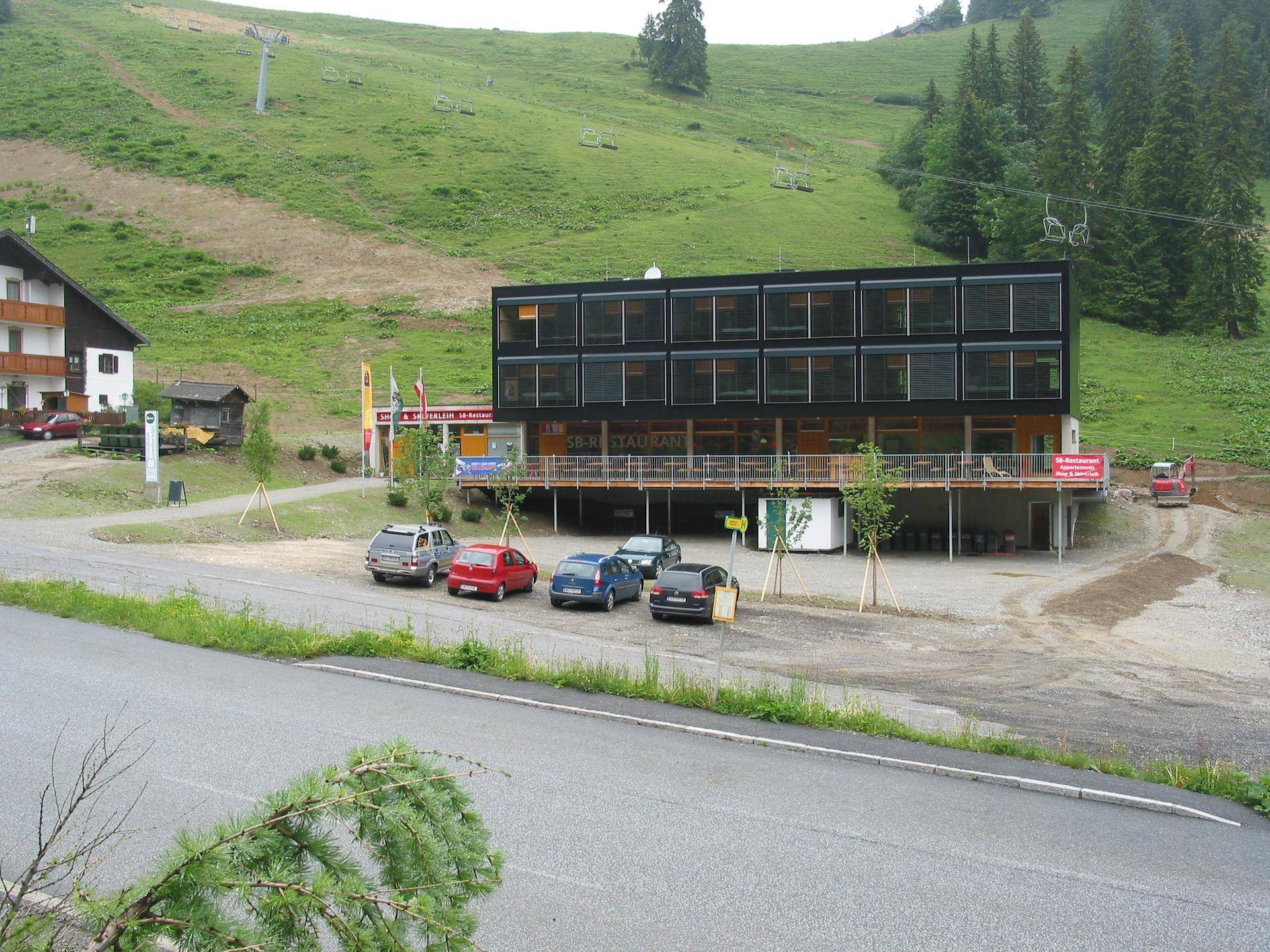 Weitläufige Außenansicht des modernen Gebäudes mit umliegender Landschaft, Straße und grünen Hängen.