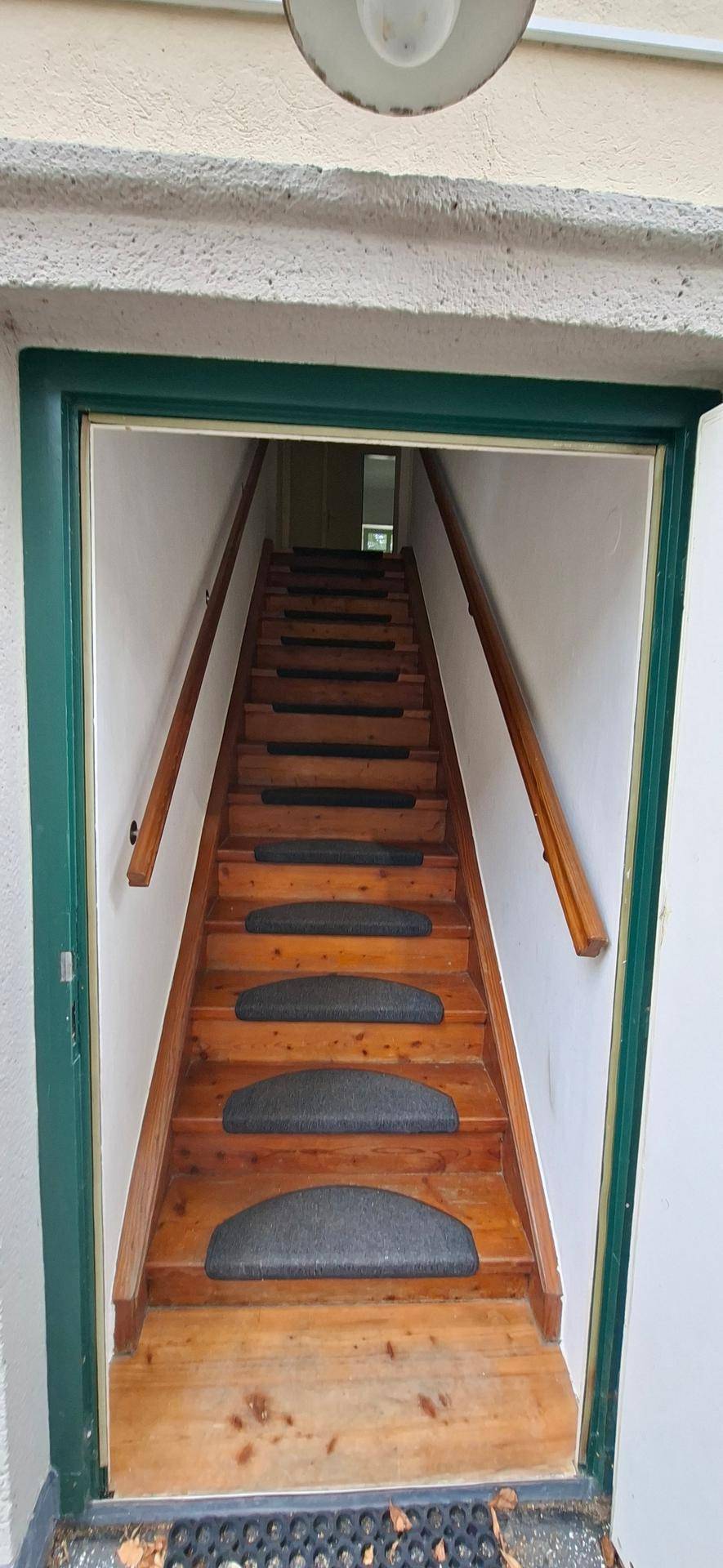 Helle Holztreppe mit Teppichstufen und Holzgeländer, die in die obere Etage führt.
