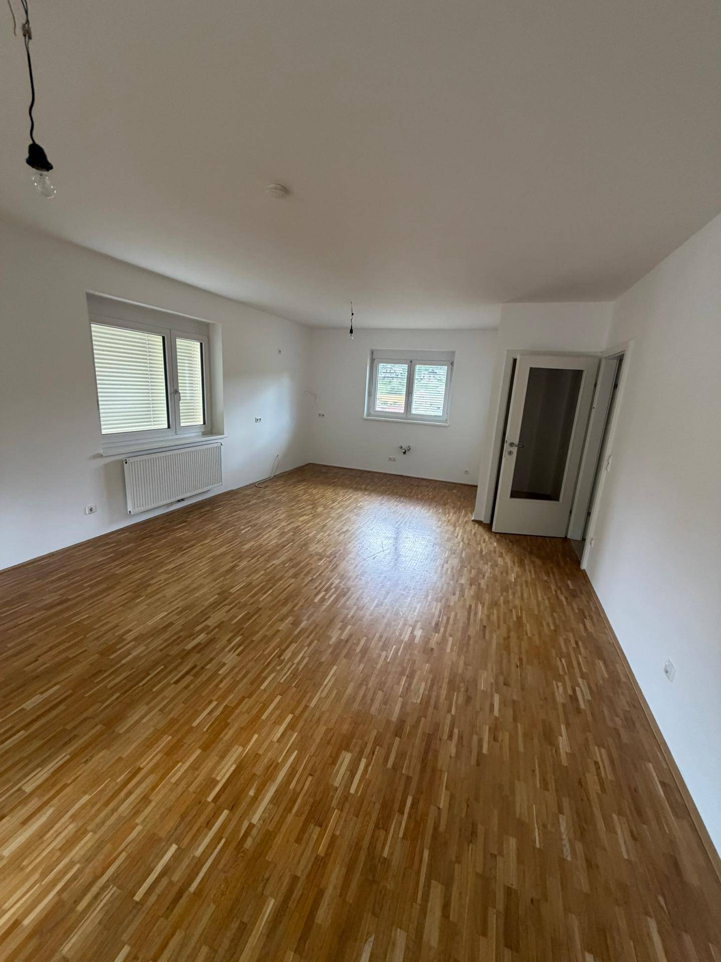 Großes, helles Wohnzimmer mit Parkettboden und mehreren Fenstern für viel Tageslicht.