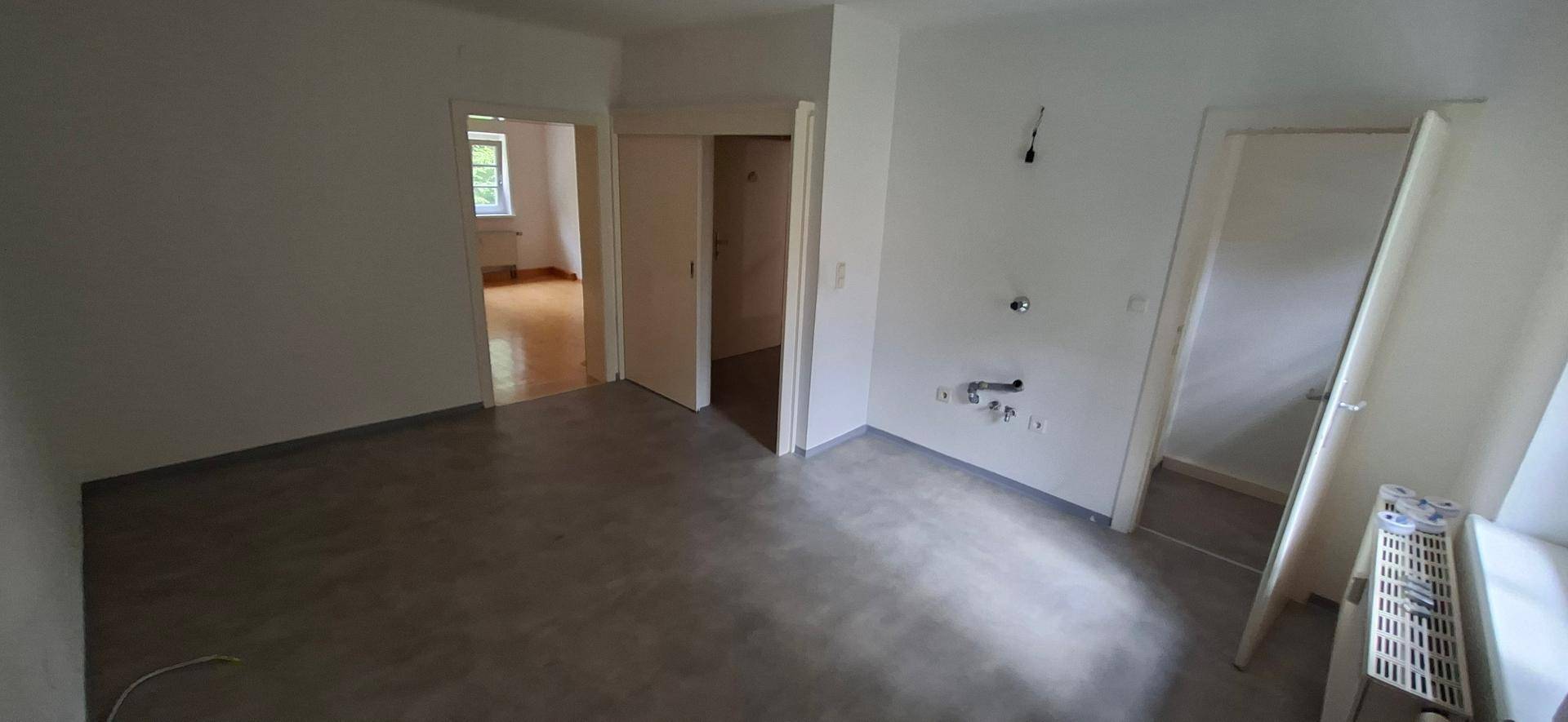 Heller Raum mit grauem Boden und Anschlüssen für eine Küche, bereit zur Installation.