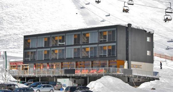 Modernes Gebäude im Winter mit schneebedeckter Umgebung und Skiliften im Hintergrund.
