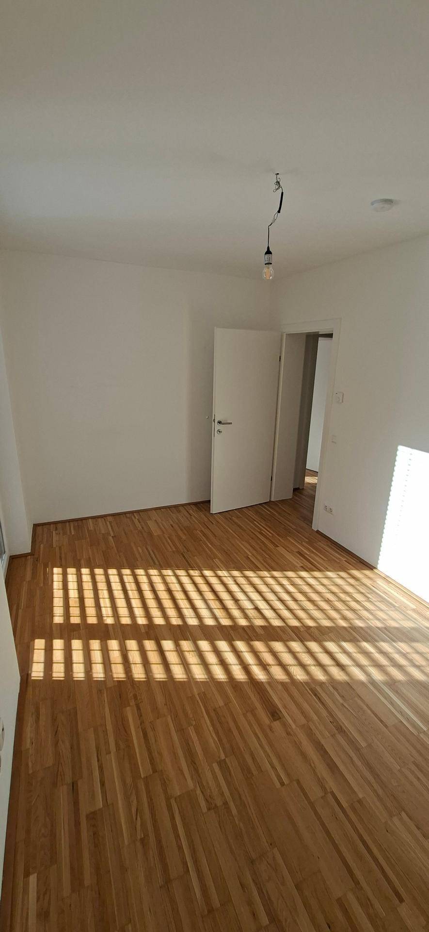 Geräumiges Schlafzimmer mit Holzparkettboden und viel Sonnenlicht, das den Raum erhellt.