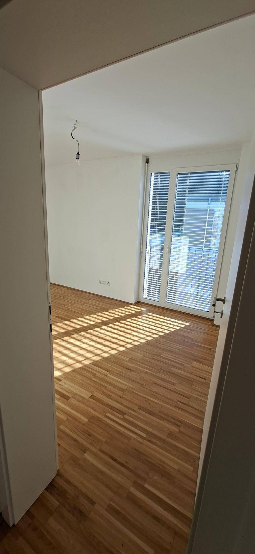 Lichtdurchflutetes Schlafzimmer mit Holzparkettboden und großen Fenstern, die eine angenehme Atmosphäre schaffen.